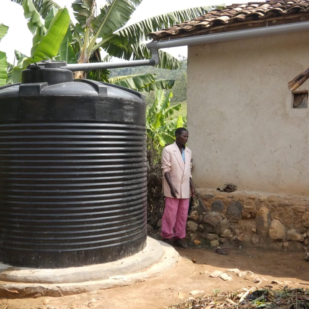 A Village of Hope participant next to his new water tank, which is connected to the house’s gutters with a pipe.